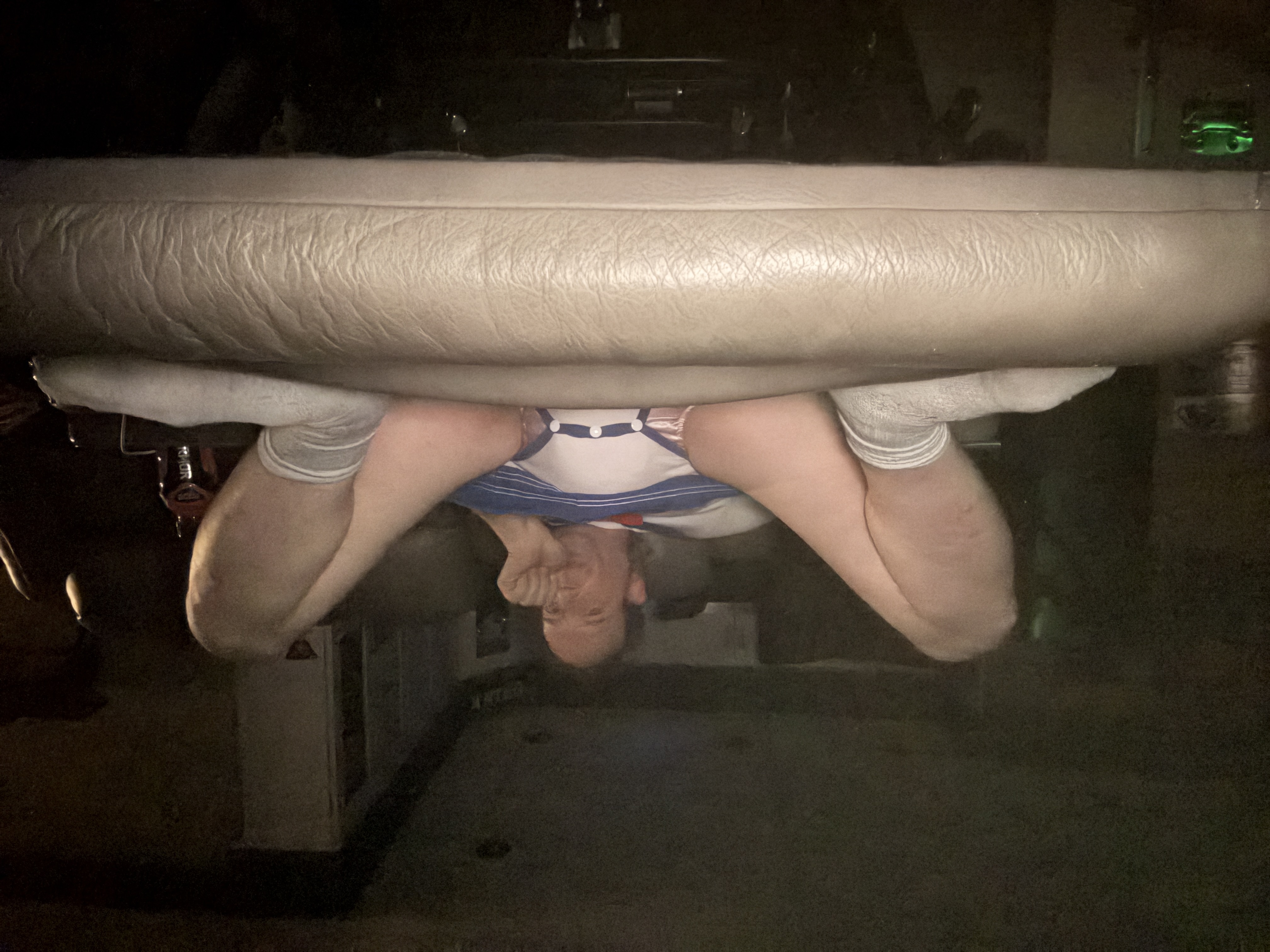 A person in a sailor-style outfit lounges on a leather couch in a dark room, feet in white socks near the camera.